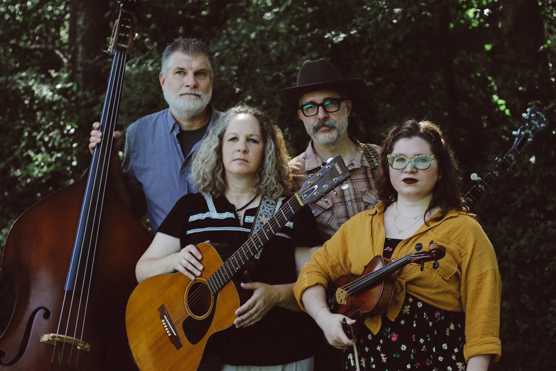 The four members of The Scrips outdoors with upright bass, guitar, banjo, and fiddle